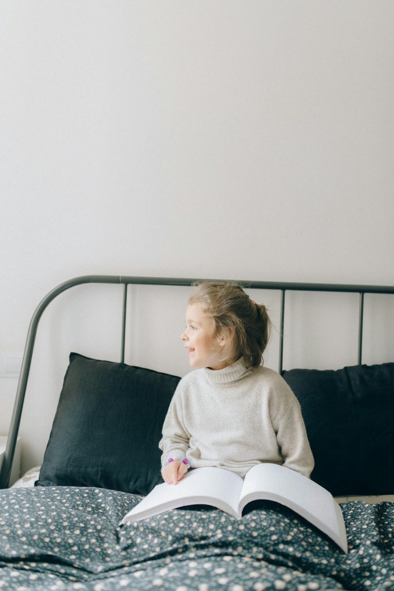 A Young Girl Sitting on the Bed while Reading Braille Book